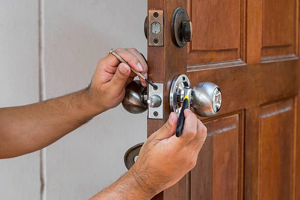 Hands repairing a door lock with tools, emphasizing locksmith services for commercial properties and security upgrades.